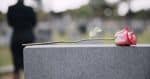 Funeral, cemetery and hands with rose on tombstone for remembrance. Trust after death concept